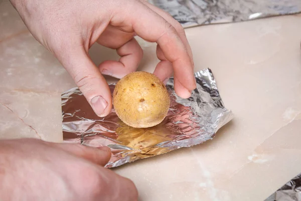 The man wraps peeled raw potatoes in foil and places them on the wire rack to bake them in oven. — Fotografia de Stock