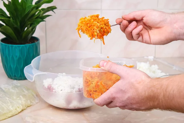 A man adds fried onions and carrots to minced meat in a bowl for lazy cabbage rolls on the table. — Fotografia de Stock