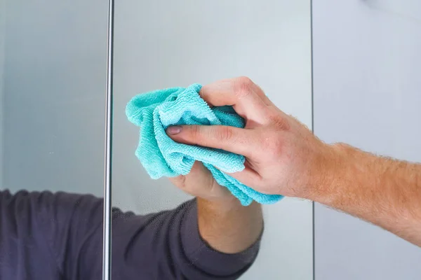 Um homem limpa um armário de espelhos na casa de banho com pano. Limpeza da casa, banheiro. — Fotografia de Stock