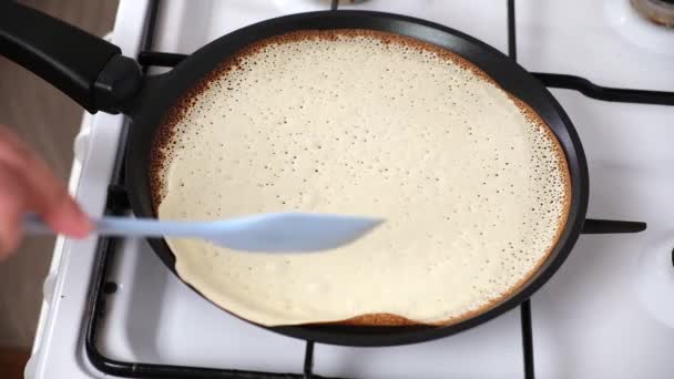 De vrouw draait de pannenkoek om in een pan. Crêpes worden gebakken in een koekenpan op het fornuis. Pannenkoeken bakken — Stockvideo
