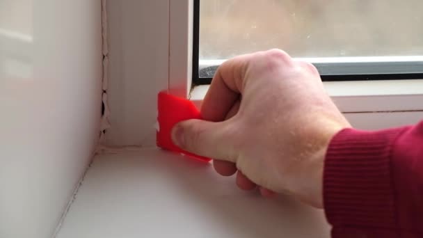 A férfi eltávolítja a szilikon tömítőanyagot az ablak és párkány között egy gumi spatulával. Gyönyörű. — Stock videók