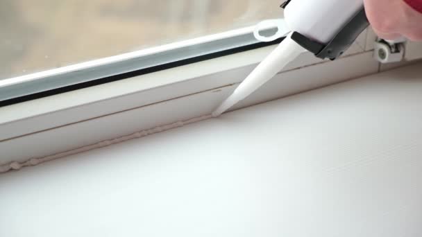 Мужчина наносит герметик на шов между окном и подоконником из тюбика силиконового уплотнителя — стоковое видео
