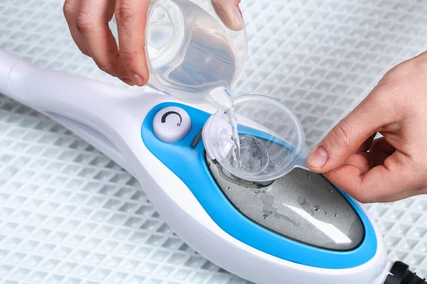 A man pours distilled water into container of a steam cleaner, steam mop. — Stock Photo, Image