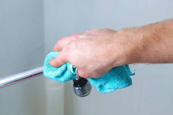 Um homem limpa uma torneira misturadora, torneira com um pano. Limpeza da casa, banheiro. — Fotografia de Stock