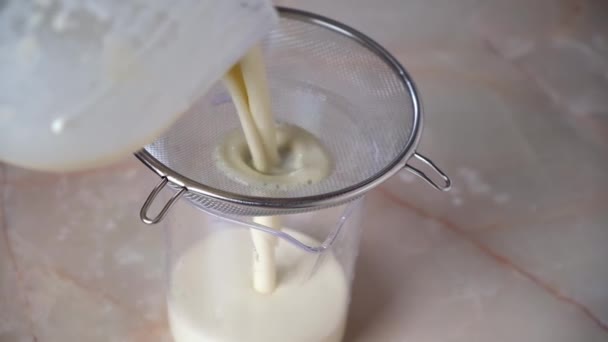 The woman is filtering the pancake dough through sieve to remove the lumps. Cooking crepes. — Vídeo de stock