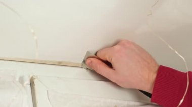 Bir adam pencere ile yamaç arasındaki eski, kurumuş, kirli dolgu macununu söker..