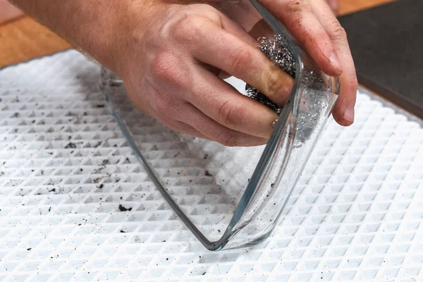 Um homem está limpando assadeira suja com uma espessa camada de carbono com um pano de ferro. Objectos de vidro — Fotografia de Stock