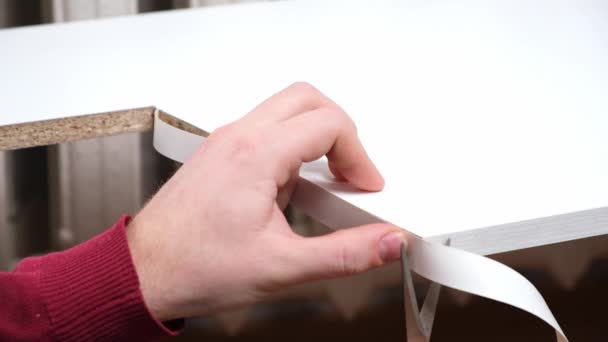 Un homme colle des bordures de mélamine blanche sur le bord brut des meubles en panneaux de particules de bois. — Video