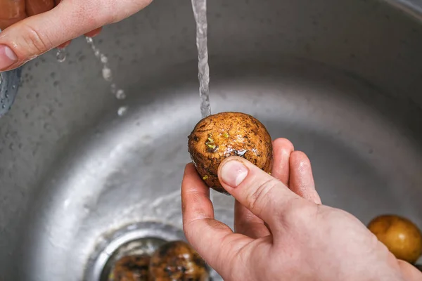 A man washes raw potatoes in sink under water to bake them in foil in the oven. — Fotografia de Stock