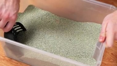 Adam çöp kutusunu temizliyor. Elin bir kepçeyi topak topak tutuyor. Kümeleme doldurucu.