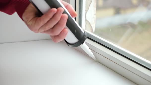Мужчина наносит герметик на шов между окном и подоконником из тюбика силиконового уплотнителя — стоковое видео