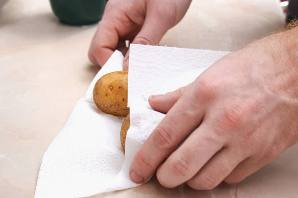 Мужчина сушит сырую, вымытую картошку бумажными полотенцами и салфетками, чтобы испечь их в фольге в духовке. — стоковое фото
