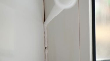 Bir adam, silikon dolgu maddesiyle pencerenin pervazı arasındaki dikişe bir mühür uyguluyor.