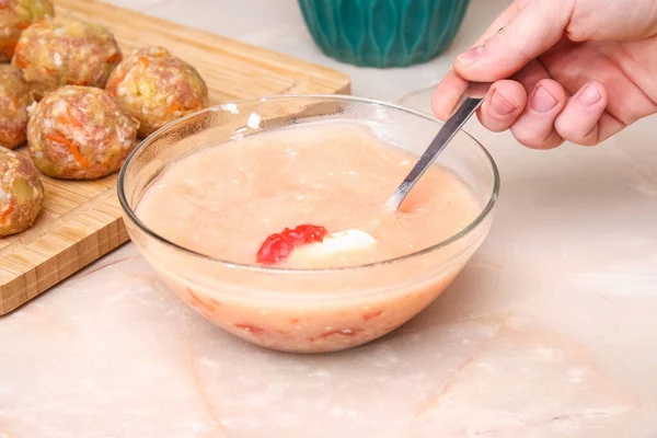 Un hombre está revolviendo la salsa con batidor para cocinar rollos de col perezosa en una olla de cocción lenta. Imágenes De Stock Sin Royalties Gratis