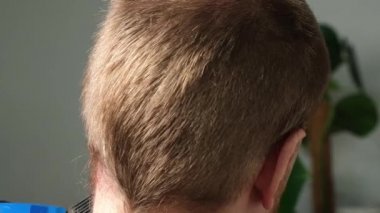 Evde bir adam elektrikli makasla saçını kestiriyor. Ev tıraşı. Bir kuaförde tasarruf.