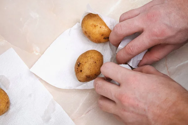 A man dries raw, washed potatoes with paper towels and napkins to bake them in foil in oven. — Fotografia de Stock