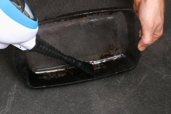 A man cleans a dirty baking dish with a thick layer of carbon with a special steam cleaner nozzle Stock Image