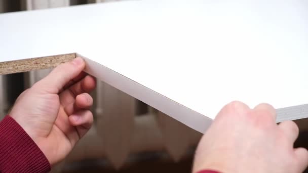 Un homme colle des bordures de mélamine blanche sur le bord brut des meubles en panneaux de particules de bois. — Video