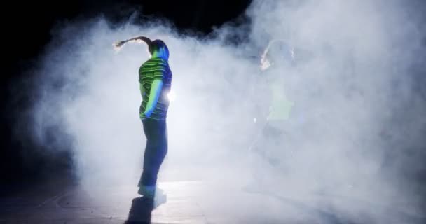 二人の若い女性ダンサーは、光と煙の背景とスローモーションでヒップホップダンスを実行 — ストック動画