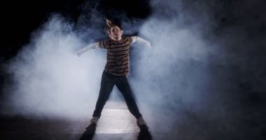 Genç bayan dansçı strop ışığı ve duman arka planıyla ağır çekimde hip hop dansı yapıyor.