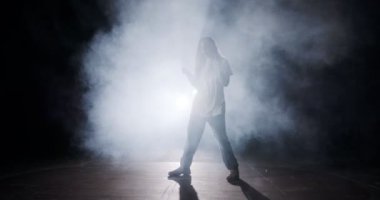 Hafif ve dumanlı ağır çekimde hip hop dansı yapan bir kadın dansçının silueti