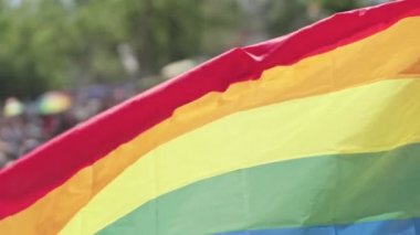 LGBTQ gökkuşağı bayrağı arka planda insanlarla ağır çekimde dalgalanıyor
