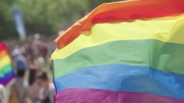 LGBTQ gökkuşağı bayrağı arka planda insanlarla ağır çekimde dalgalanıyor