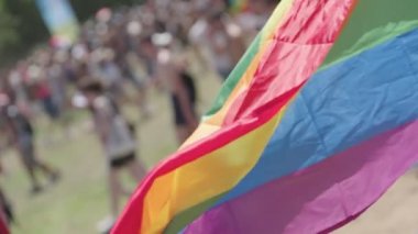 LGBTQ gökkuşağı bayrağı arka planda insanlarla ağır çekimde dalgalanıyor