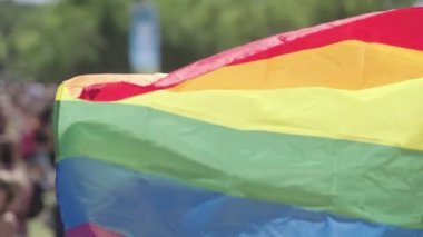 LGBTQ gökkuşağı bayrağı arka planda insanlarla ağır çekimde dalgalanıyor
