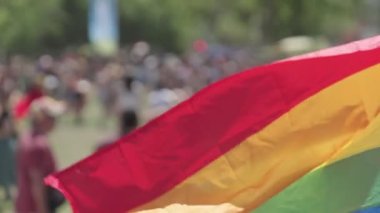 LGBTQ gökkuşağı bayrağı arka planda insanlarla ağır çekimde dalgalanıyor