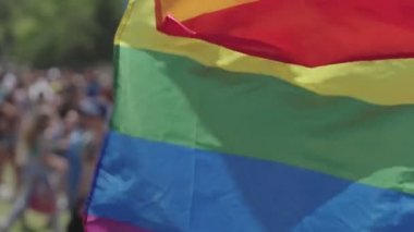 LGBTQ gökkuşağı bayrağı arka planda insanlarla ağır çekimde dalgalanıyor
