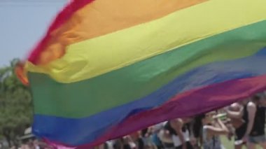 LGBTQ gökkuşağı bayrağı arka planda insanlarla ağır çekimde dalgalanıyor