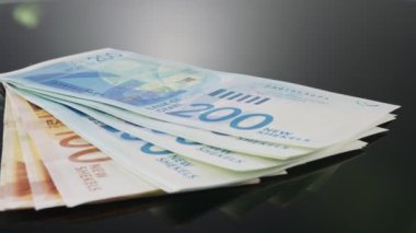 Bills and coins of New Israeli Shekels rotating on reflective surface