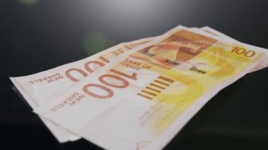 Bills and coins of New Israeli Shekels rotating on reflective surface