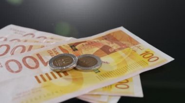 Bills and coins of New Israeli Shekels rotating on reflective surface