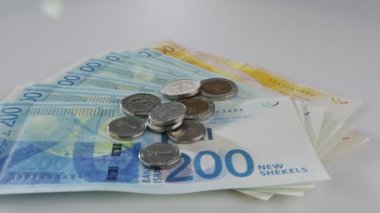 Bills and coins of New Israeli Shekels rotating on reflective surface