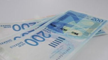 Bills and coins of New Israeli Shekels rotating on reflective surface