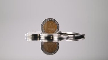 Coins of New Israeli Shekels rotating on reflective surface