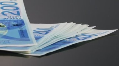 New Israeli Shekels bills falling on a reflective surface