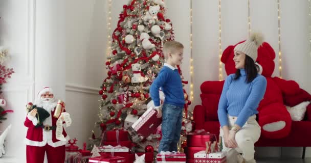 A preschool son gives a happy mom a New Years gift. Lonely mother with her son near a decorated Christmas tree, holiday, congratulations, small child, cheerful laughter. — Video Stock