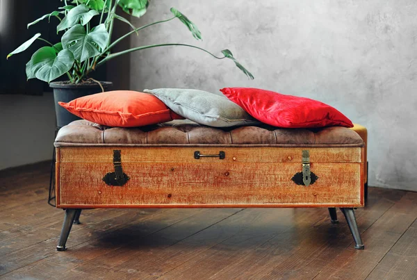 Cajonera retro de madera con almohadas rojas, junto a una planta verde cerca de una pared gris en el interior. Diseño de interiores. —  Fotos de Stock