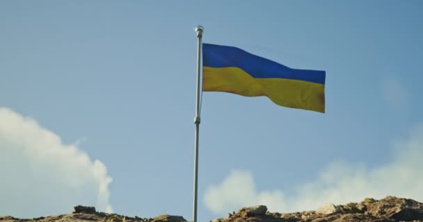 The Ukrainian flag flutters in the wind with a highly detailed fabric texture. Flag of Ukraine on a mountain against the sky, the camera slowly approaches it. — Stock Video