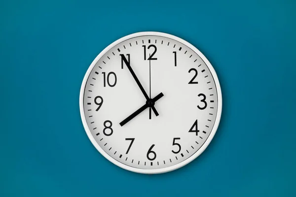 Белые настенные часы висят на голубой стене с копировальным пространством и центральной композицией. — стоковое фото