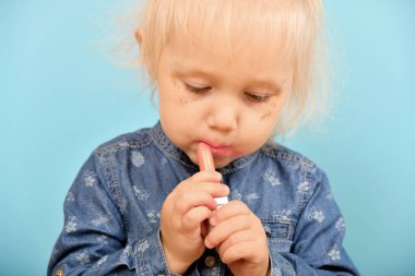 Küçük kız dudaklarını kırmızı rujla boyuyor. Cazibe, kadınlık ve çekicilik kavramı..