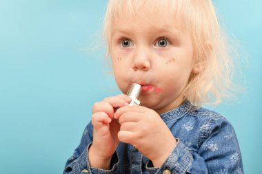 Çocuk gizlice ve beceriksizce dudaklarını Maya kırmızı rujuyla boyuyor..