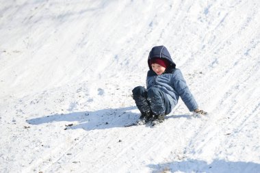 Çocuk poposunun üstüne oturur ve kaygan bir kar kaydırağının üzerinde ayakları üzerine iner..