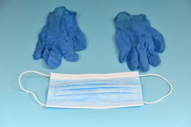 Mavi arka planda tıbbi maske ve mavi eldivenler var. Virüs koruma ve koruma kavramı.