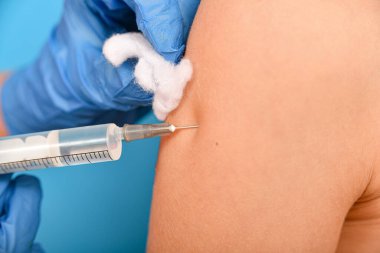 Çocukların aşılanması için. Doktor çocuğa aşı yapar ve omzunu pamukla siler..