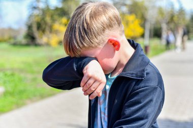 Oğlan ağlar ve gözyaşlarını siler. Parkta yürürken elleri sokakta..