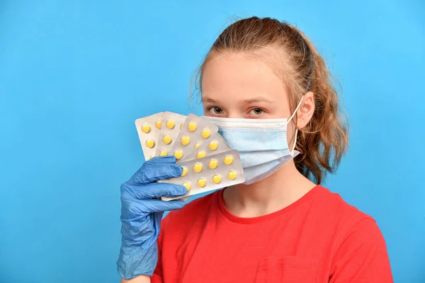 一个戴着防护面具和蓝色医疗手套的女孩手里拿着药丸泡 满脸都是药丸 — 图库照片